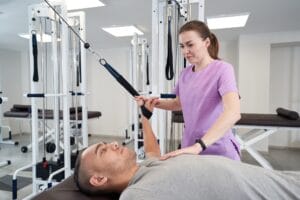 PT practice session showing a physical therapist assisting a patient with a dumbbell chest press on a bench.
