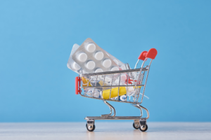 Shopping trolley cart with medicine pills on the blue background. Health care and medicine concept